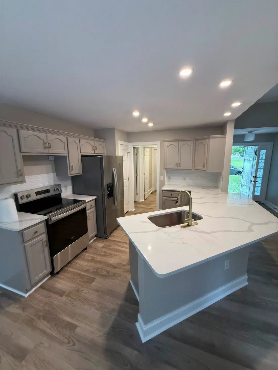 Finished kitchen with a quartz peninsula, brass faucet, greige cabinets and vinyl plank floor