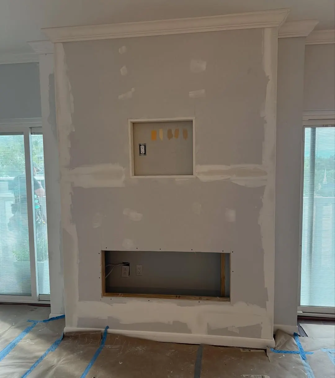 Drywall installed on the fireplace wall with openings for TV and fireplace