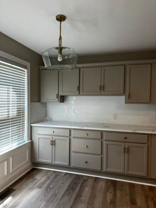 Finished kitchen wall with greige cabinets, brass pulls and a wavy white tile backsplash